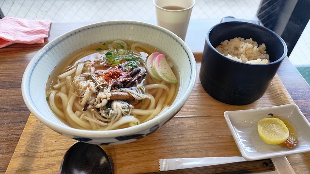 山菜うどんセットの写真。漬物のたくあんには梅肉が添えられている。箸、おたま、使い捨てナプキン付き。
