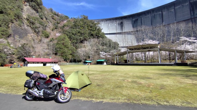 巨大なダムを背に下北山スポーツ公園キャンプ場のフリーサイトでテントとバイクが停まっている画像。